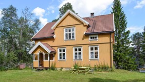 A two-story wooden house with a red-tiled roof, a porch, and a small garden with a table and chairs. - Awesome home in Tufsingdalen (Tufsingdalen)