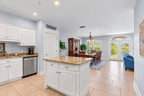 A spacious kitchen with white cabinetry, a granite countertop, and a dining area with a wooden table and chairs.