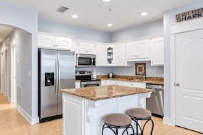 A modern kitchen with white cabinetry, stainless steel appliances, granite countertops, and a central island with stools.