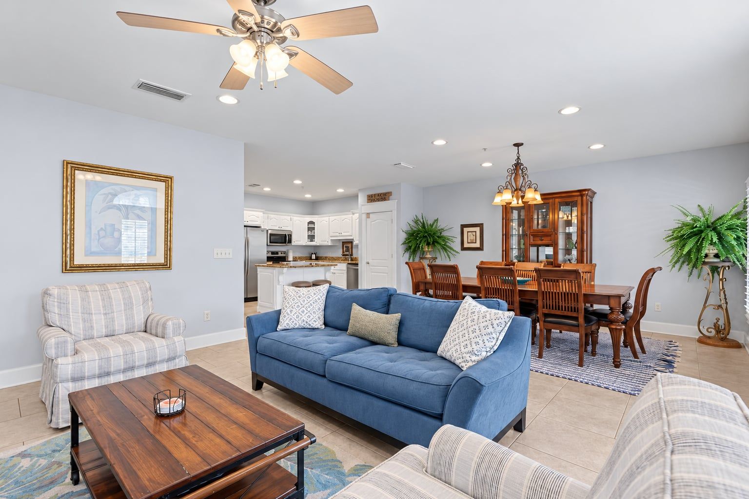 A living room with a blue sofa, a wooden coffee table, a dining area with a wooden table and chairs, and a kitchen in the background.