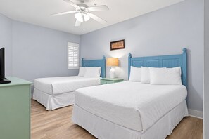 A bedroom with two beds, a ceiling fan, a nightstand with a lamp, and a television on a stand.