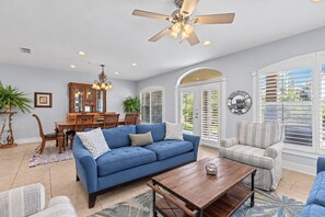 A spacious living room with a blue sofa, a wooden coffee table, and a striped armchair.