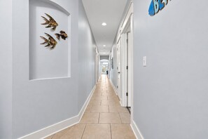 A hallway with a light-colored floor, white walls, and a series of doors on one side.