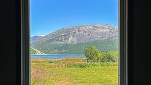 En utsikt från ett fönster över ett bergigt landskap med en bro, klar himmel och en gräsklädd förgrund.