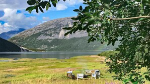 Ett lugnt utomhusområde med sittplatser och utsikt över en sjö och berg.