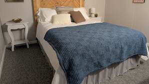 Un dormitorio con cabecera de madera, manta azul y mesita de noche con un cuenco.