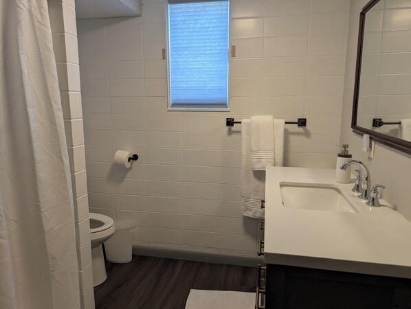 A bathroom with a toilet, a sink, a mirror, and a window.
