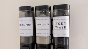 Tres recipientes etiquetados como champú, acondicionador y gel de baño.