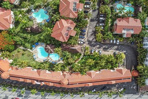 Eine Vogelperspektive eines Resorts mit mehreren Schwimmbecken, Palmen und einem großen Gebäude mit rotem Ziegeldach.