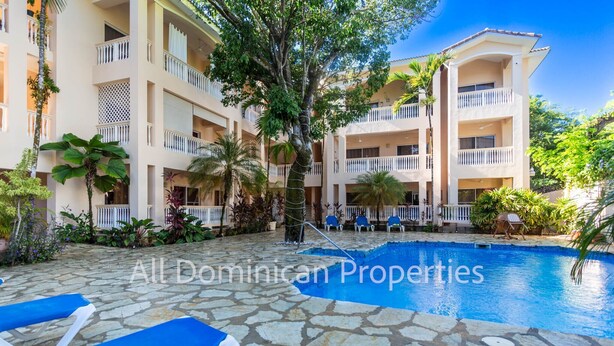 A multi-story hotel with a swimming pool, outdoor seating, and lush landscaping.