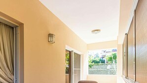 A spacious room with a sliding glass door leading to a balcony, a comfortable chair, a small table, and a wall-mounted light fixture.