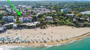An aerial view of a coastal area with a beach, buildings, and a green arrow pointing to a specific location.