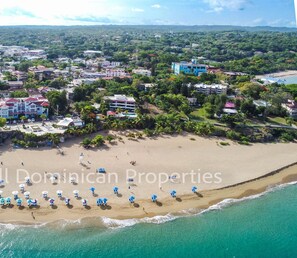 An aerial view of a coastal area with a beach, buildings, and a green arrow pointing to a specific location.