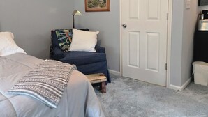 Una camera da letto con un letto, un divano blu, un tavolino, una porta bianca e un quadro appeso al muro.