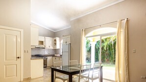 A kitchen with white cabinets, a dining table with chairs, and a view of greenery outside. - Sosua Ocean Village, villa 19a (Sosúa)
