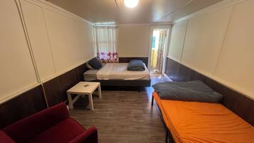 A compact room with two beds, a small table, and a red chair.