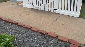 Une maison à deux étages avec une clôture en bois peinte en blanc, un porche à l’avant et un escalier menant au deuxième étage.