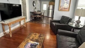 Un salon avec une table basse en bois, un canapé en cuir noir, un téléviseur et un ventilateur de plafond.