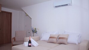 A modern bedroom with a beige sofa, a wooden chair, a small table with a bottle and flowers, and an air conditioning unit on the wall. - Apartment in Cartagena (Cartagena de Indias)
