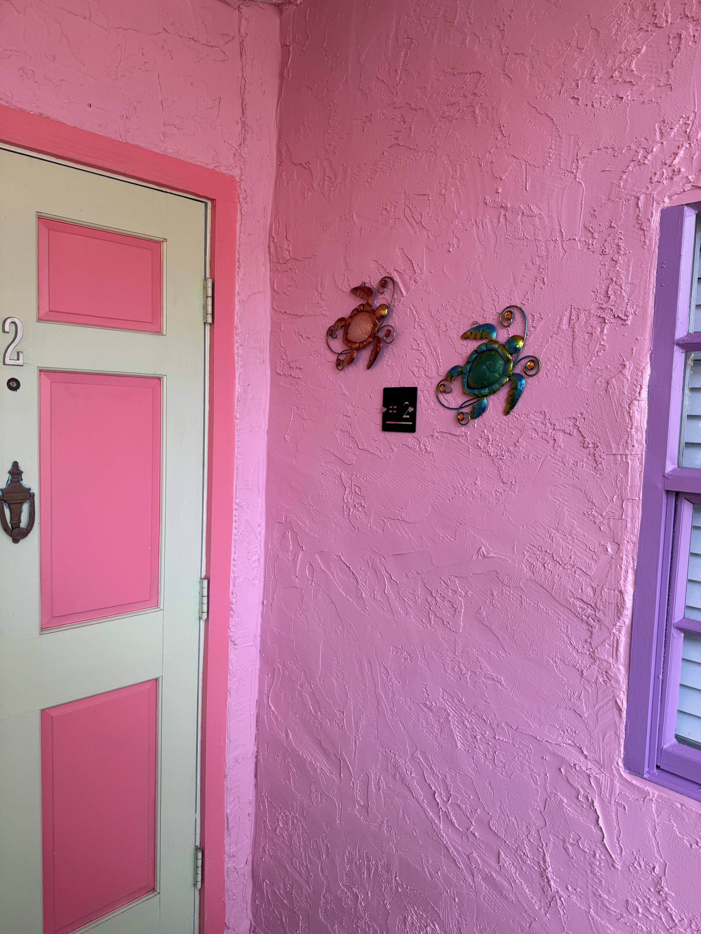 Una puerta rosa con el número 2 y una pequeña señal negra con un símbolo.