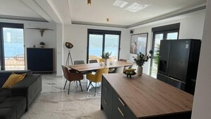A modern kitchen with a wooden island, dark cabinets, and a large refrigerator. There is a dining area with a table and chairs, and a sofa in the living area. - Penthouse apartment with sea view and pool area (Đenovići)