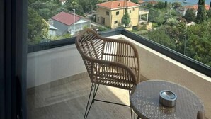 A balcony with a wicker chair and a small table, overlooking a coastal town and the sea. - Penthouse apartment with sea view and pool area (Đenovići)