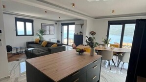 A modern living room with a wooden island, a sofa, and a dining area with a view of the sea. - Penthouse apartment with sea view and pool area (Đenovići)