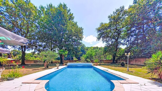 A rectangular swimming pool with a tiled deck surrounding it, set in a landscaped garden with trees and a clear sky. - Maison du Chêne Pointu by Interhome (Saint Pandelon)