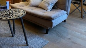 A cozy living room with a sofa, a small round table, and a kitchen in the background. - El Alba Descanso (Patate)
