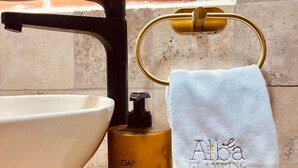 A bathroom with a white vessel sink, a black faucet, a gold soap dispenser, and a towel with "Alba GLAMPTING" text. - El Alba Descanso (Patate)