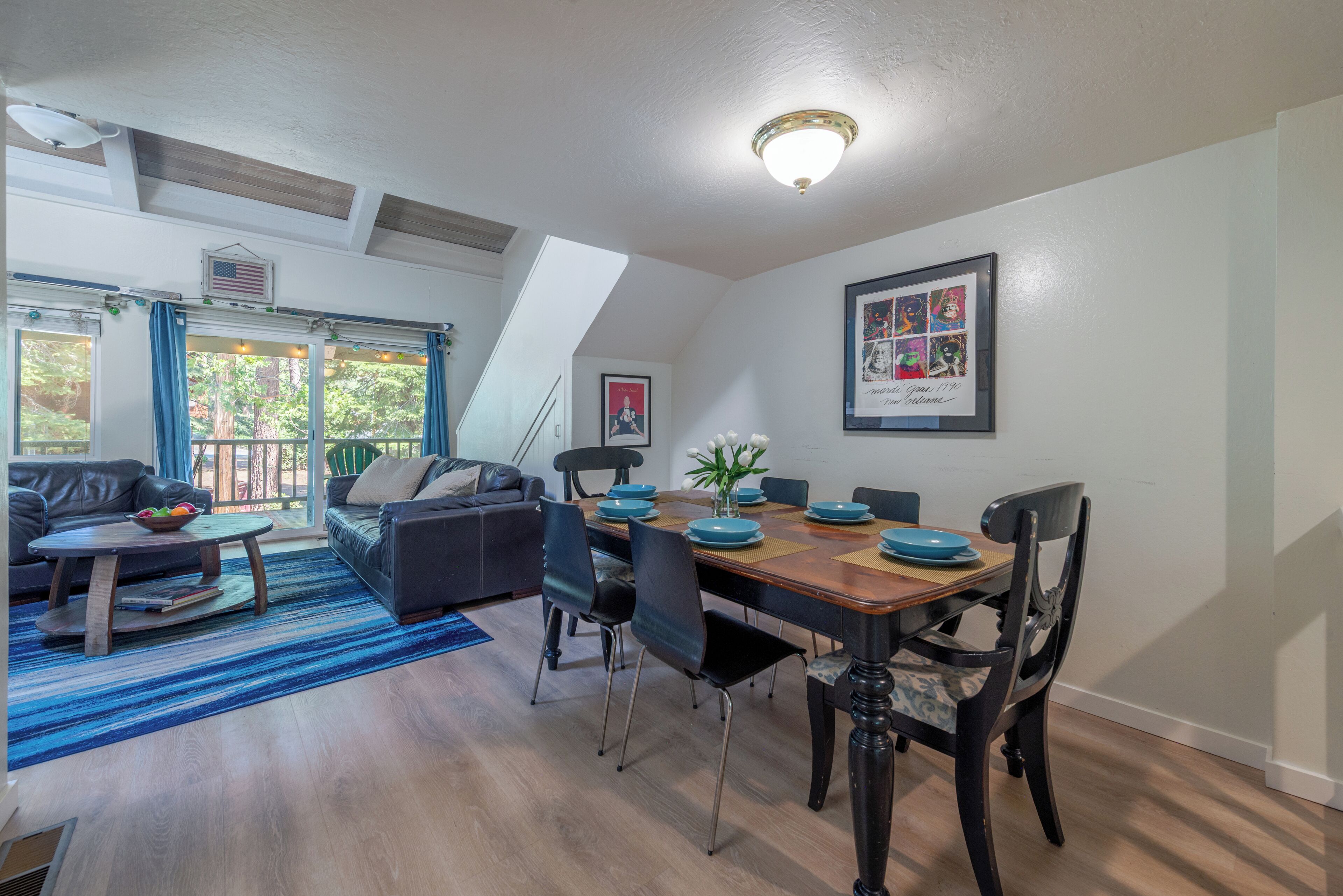 A modern living room with a dining area, featuring a wooden dining table, blue chairs, a sofa, and a coffee table.