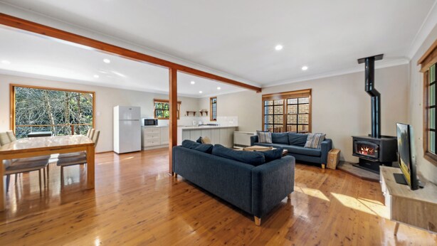 A spacious living area with a wooden floor, a sofa, a dining table, and a kitchen in the background.