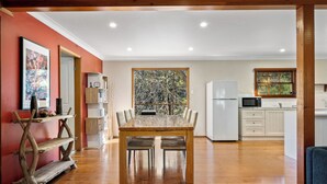 A spacious dining area with a wooden table and chairs, a kitchen with white cabinets, and a large window with a view of trees.