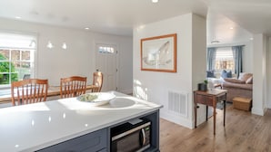 A modern kitchen with a central island, dining area with wooden chairs, a framed fish artwork on the wall, and a cozy living area with a sofa and cushions. - Chimney Corner- Keswick Home Close to Vineyards (Keswick)