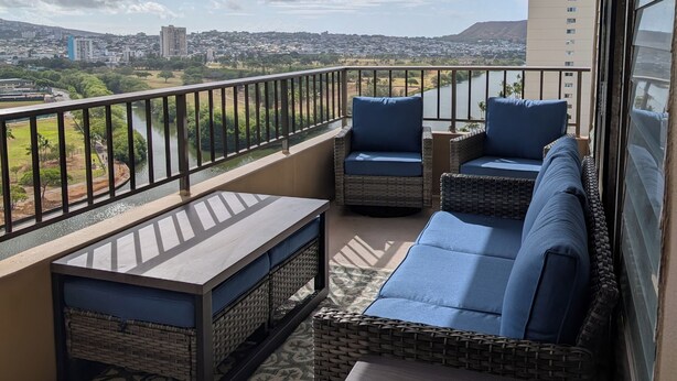 A balcony with wicker furniture, a view of a cityscape, and a river. - Newly renovated, secure, 2-bedroom apartment in beautiful Waikiki with AC (Honolulu)