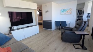 A modern living room with a flat-screen TV, grey sofa, and a black coffee table. - Newly renovated, secure, 2-bedroom apartment in beautiful Waikiki with AC (Honolulu)
