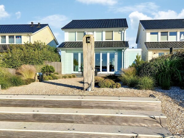 Une propriété située en bord de mer, avec une promenade en bois menant à une maison bleu clair dotée d’un toit foncé.