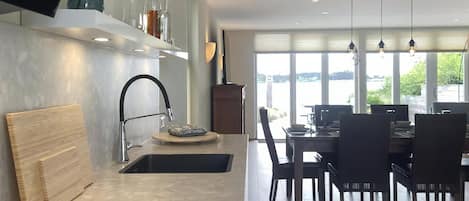 A modern kitchen with a built-in sink, a dining area with a table and chairs, and a view of the outdoors through large windows.