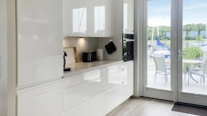 Une cuisine moderne avec des meubles blancs, un plan de travail noir et une vue sur l’espace extérieur aménagé, visible à travers une porte vitrée.