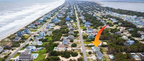 An aerial view of a coastal residential area with houses, roads, and a beach.