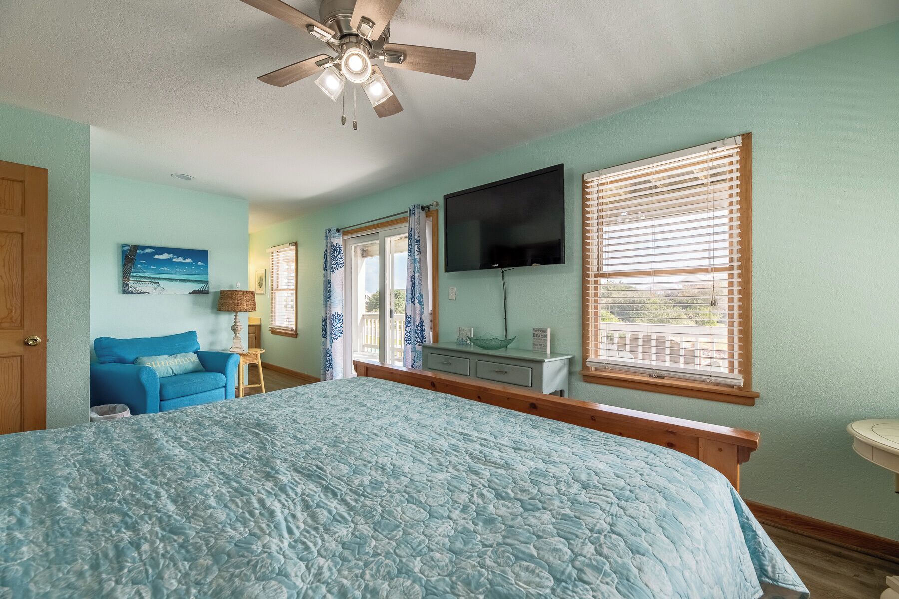 A bedroom with a bed, a ceiling fan, a TV, and a window with blinds.