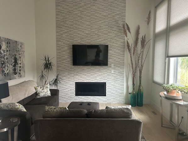A modern living room with a brick-patterned wall, a flat-screen TV, a sofa, a coffee table, and a side table with a lamp.