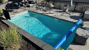 A clear blue pool with a slide, surrounded by lounge chairs and a deck area with a view of the mountains.