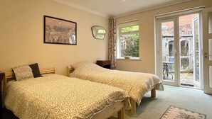 A bedroom with two beds, a framed picture on the wall, a window with curtains, and a door leading to an outdoor area. - Farnham Haven: Unique Home with Courtyard (Farnham)