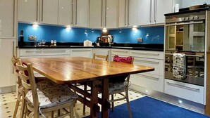 A modern kitchen with white cabinets, a blue backsplash, and a wooden dining table with chairs. - Farnham Haven: Unique Home with Courtyard (Farnham)