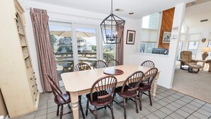 A dining area with a large table and six chairs, a hanging light fixture, and a view of the outside through large windows. - Resort Amenities, Community Pools, Hot Tub-645, Cohasset II (Corolla)