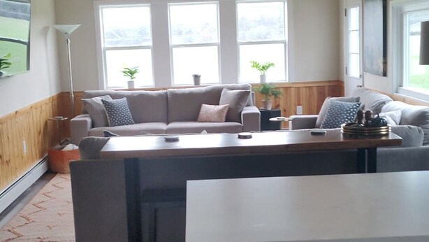 Uma sala ampla com teto de madeira, uma janela grande, sofá, mesa de jantar e área de cozinha.