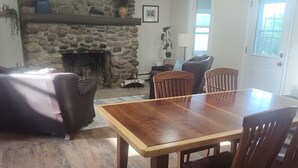 Uma área de refeições com uma mesa e cadeiras de madeira, lareira de pedra, ventilador de teto e uma porta com janela.
