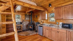 A cabin interior with a stone fireplace, wooden cabinets, a kitchen with a sink and microwave, and a wooden floor. - Phantom Canyon Resort (Victor)