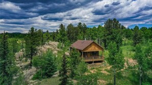 A wooden cabin with a balcony, surrounded by dense forest and a rocky landscape under a cloudy sky. - Phantom Canyon Resort (Victor)